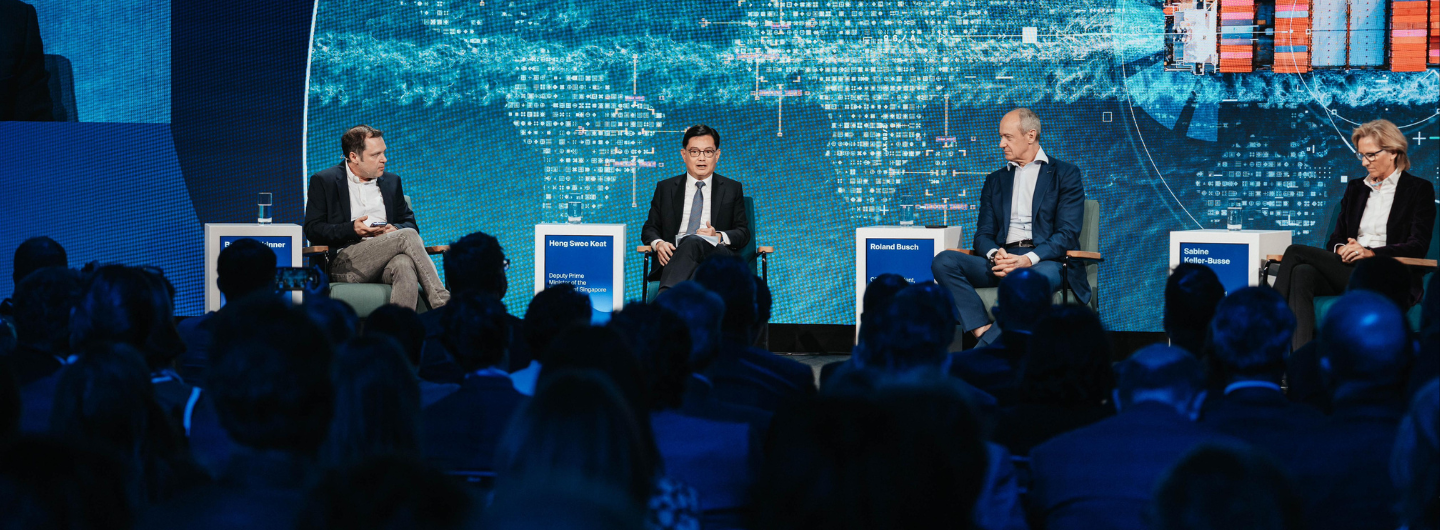 Panel with four speakers, "Heng Swee Keat" among them, before a crowd and screen backdrop.